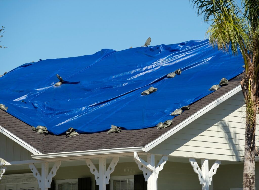 Emergency response crew installing a protective roof tarp on a residential home