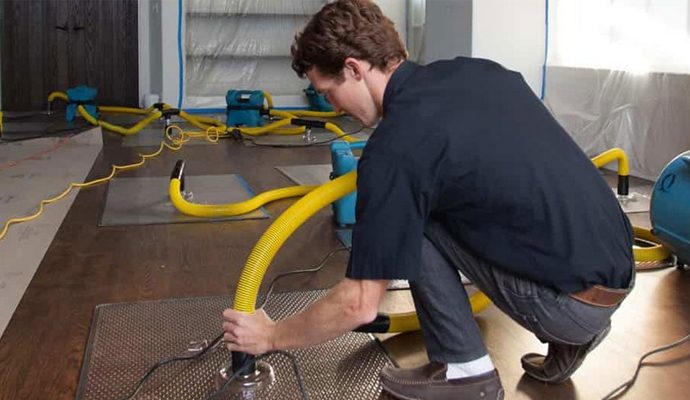Emergency water damage restoration technician setting up drying equipment in a home