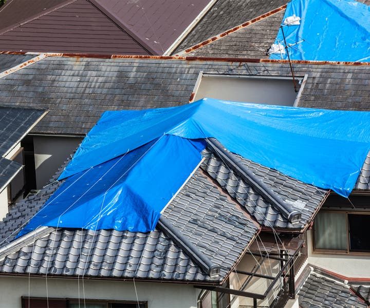 Emergency response team installing a blue protective tarp over a damaged residential roof