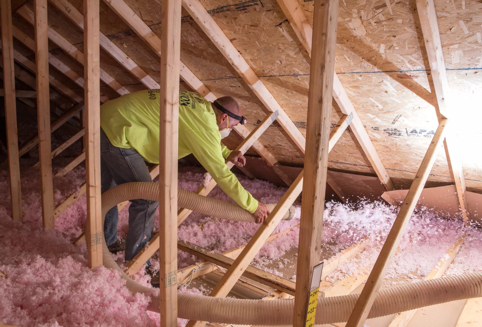 Contractor installing fiberglass batt insulation in an attic space