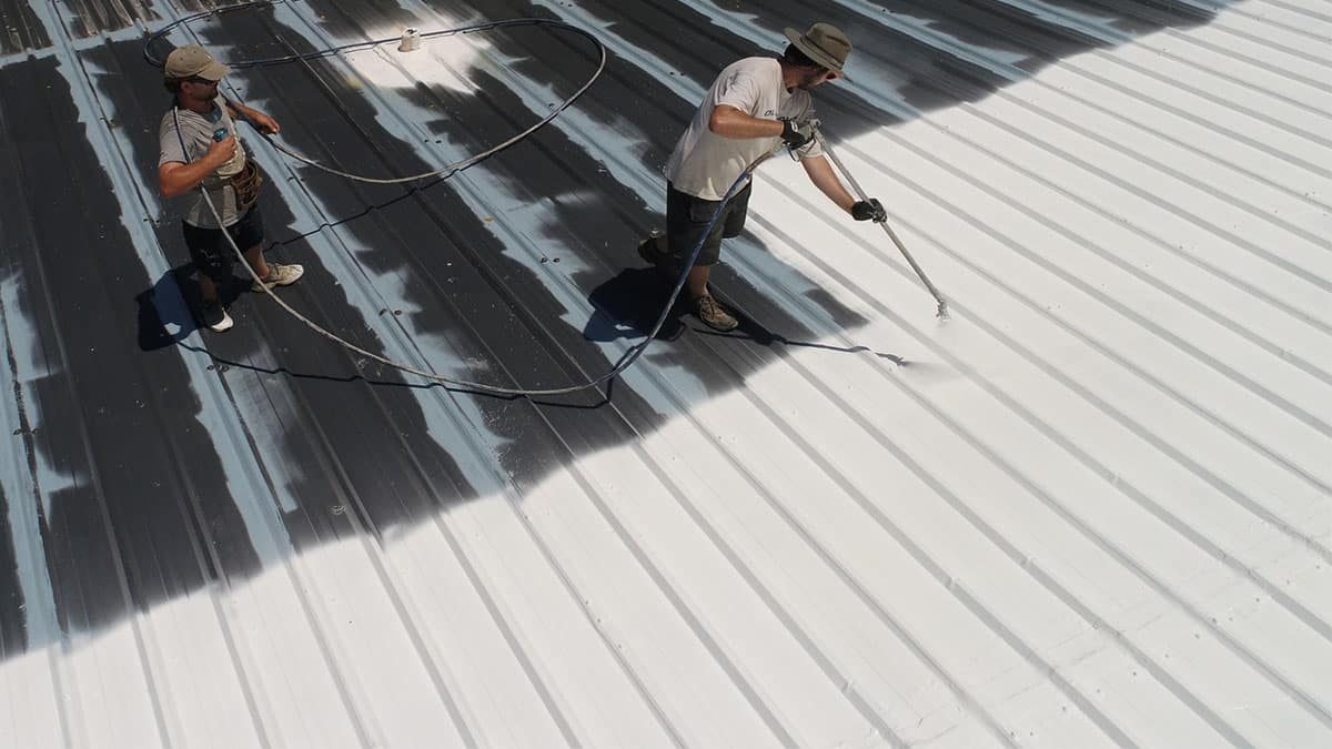 Contractors applying white reflective cool roof coating to a commercial roof