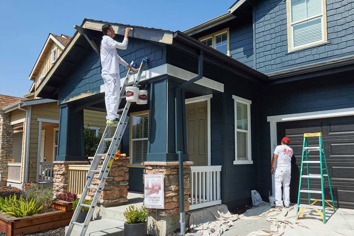 Painter on a ladder applying fresh paint to the exterior of a residential home