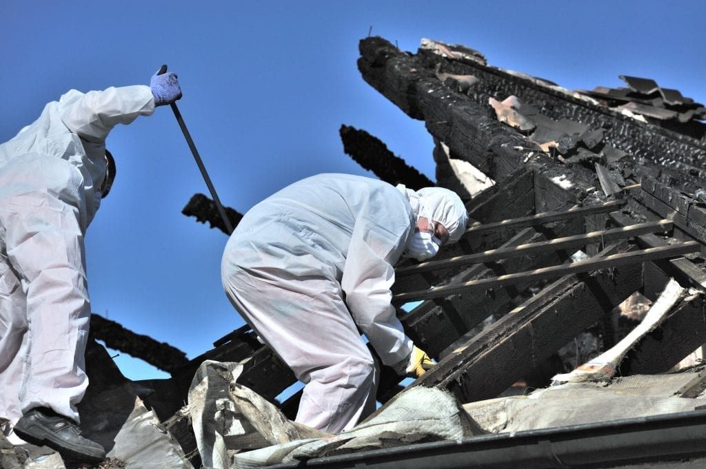 Restoration technicians in protective gear removing debris from a fire-damaged roof