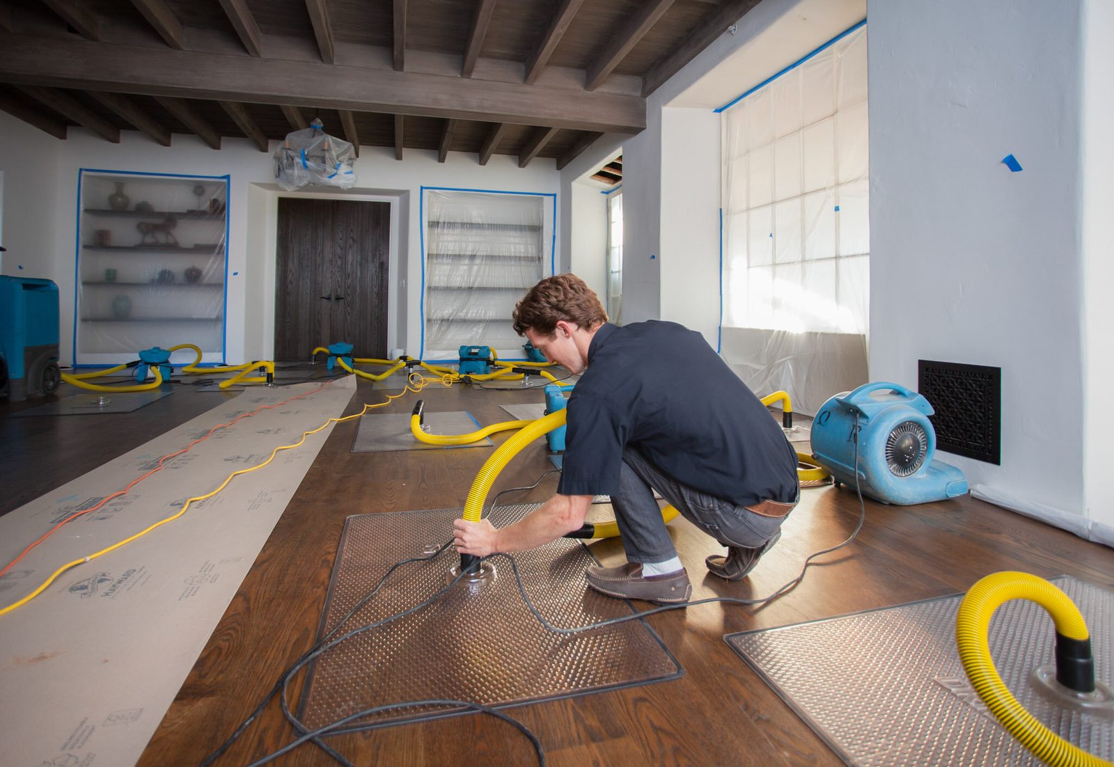 Technician using a yellow hose for flood and water restoration in a residential home