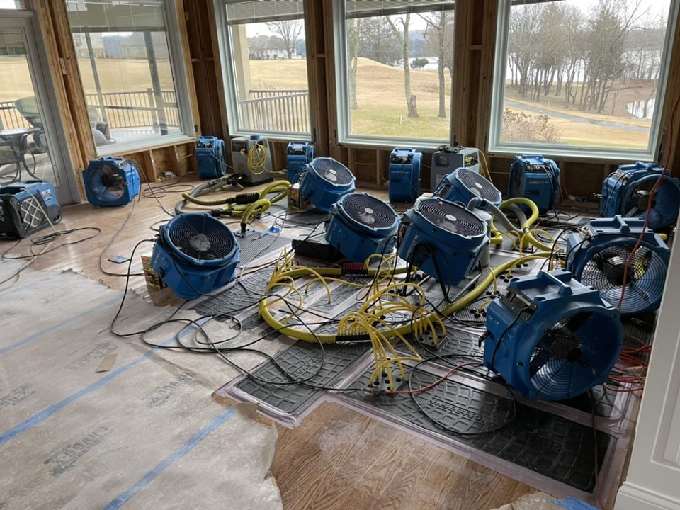 Multiple drying fans and dehumidifiers operating in a flooded room for water restoration