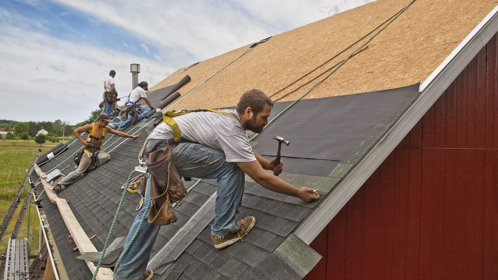 Contractors installing asphalt shingles on a steep residential roof