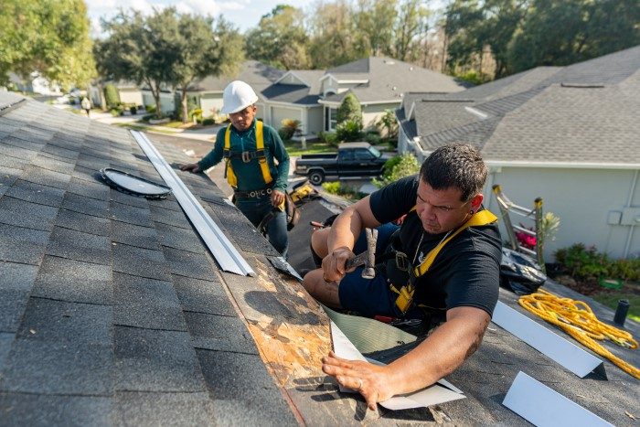 Roofing contractor using a nail gun to install new asphalt shingles