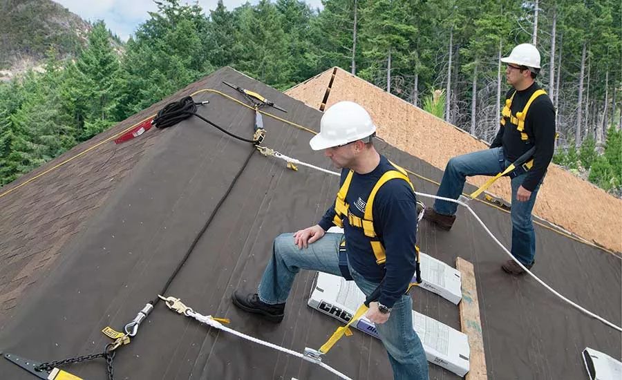 Professional roofers working on a steep roof installation with safety harnesses