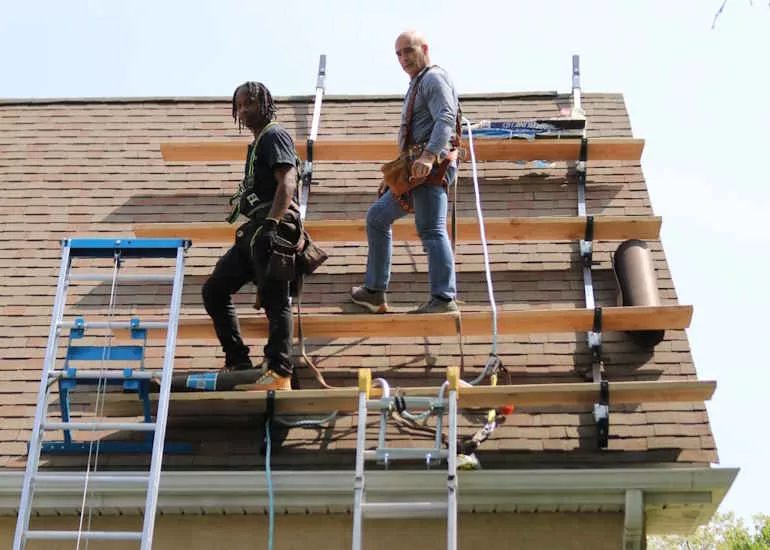 Roofing contractors working on scaffolding during a residential roof replacement